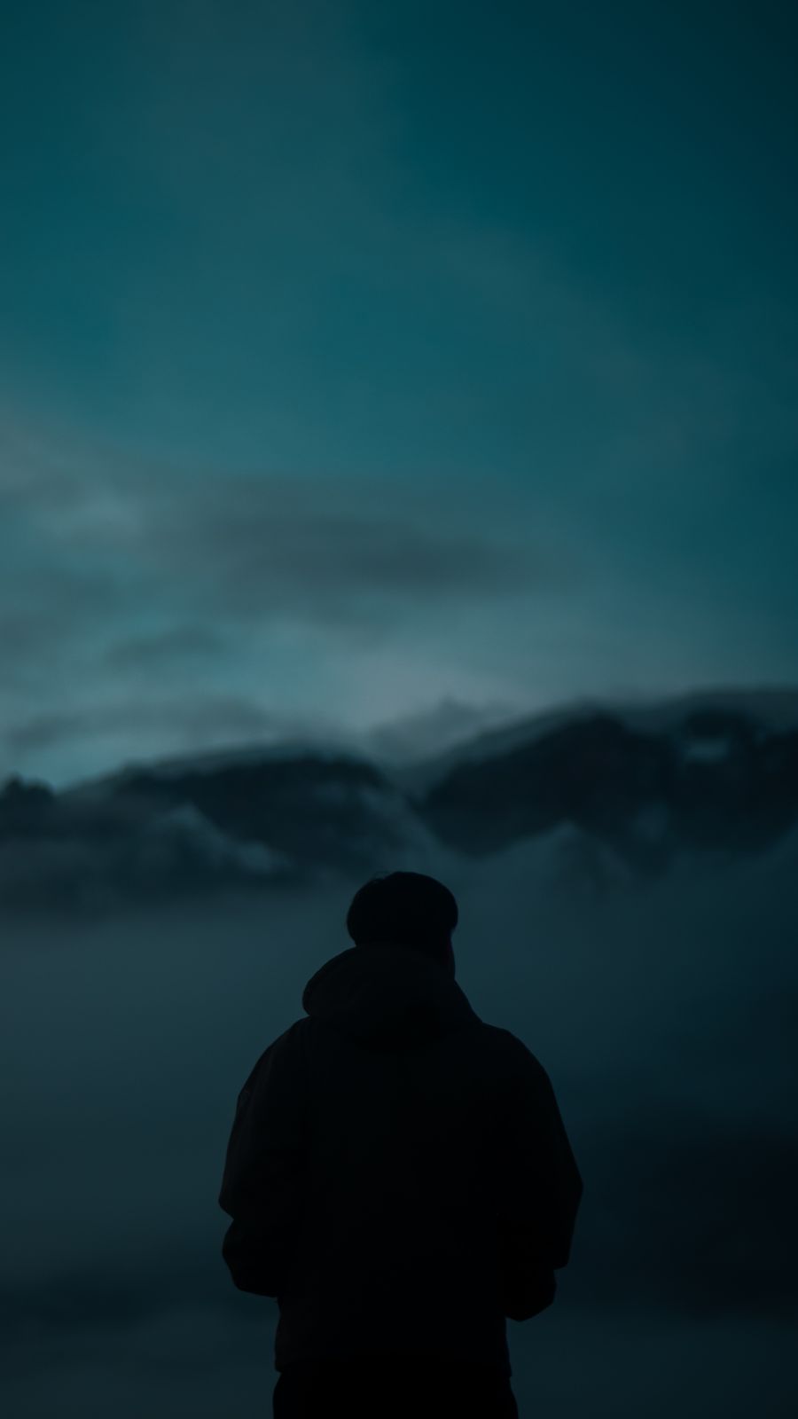 A man seen from behind, facing mountains buried in cloud